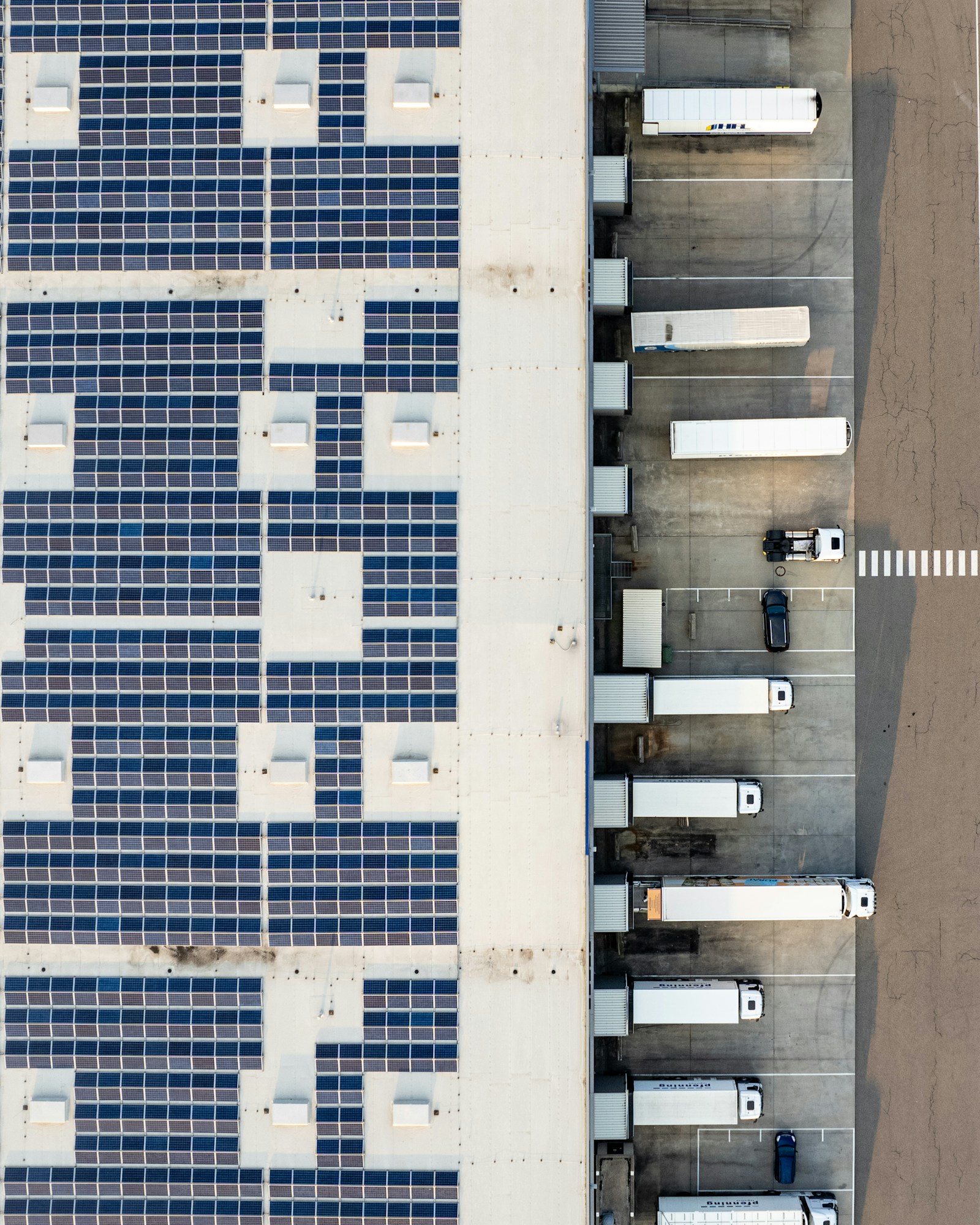 Top-down aerial of a modern distribution building with solar roof and trucks at the loading docks